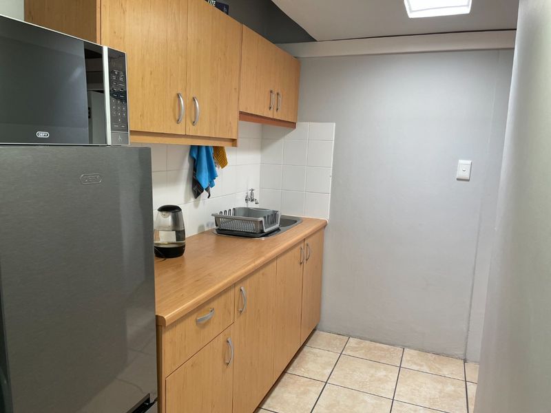 A compact kitchen area featuring light wood-finish cabinetry, laminate countertops, a stainless steel sink, and neutral ceramic floor tiling.