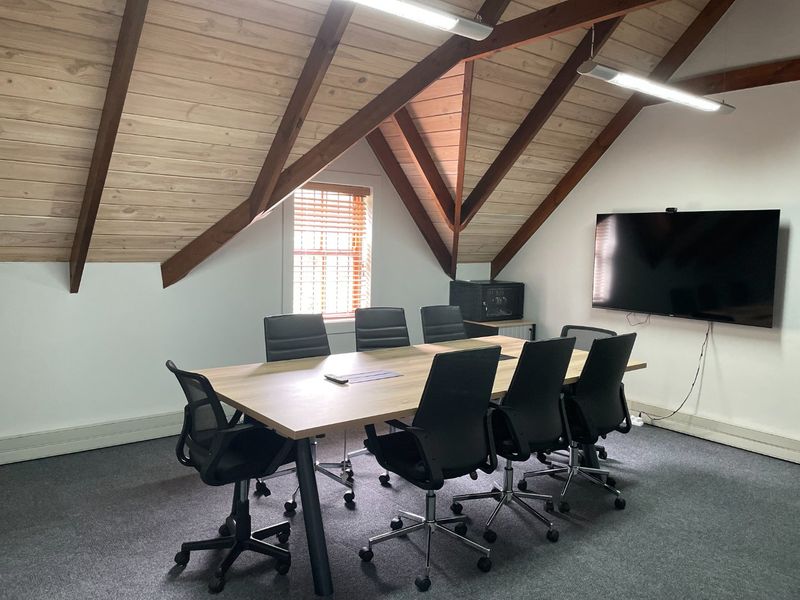 A professional meeting room featuring exposed timber rafters, a vaulted timber ceiling, carpeted flooring, and a wall-mounted television for presentations.