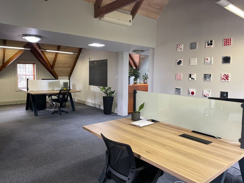 A professional office space featuring exposed timber roof trusses, carpeted flooring, and integrated glass partition screens for a modern, functional workspace.
