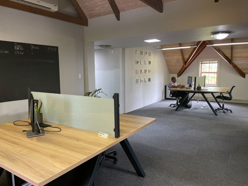 A modern, open-plan office space featuring exposed timber rafters, carpeted flooring, and a built-in chalkboard, providing a professional and functional work environment.