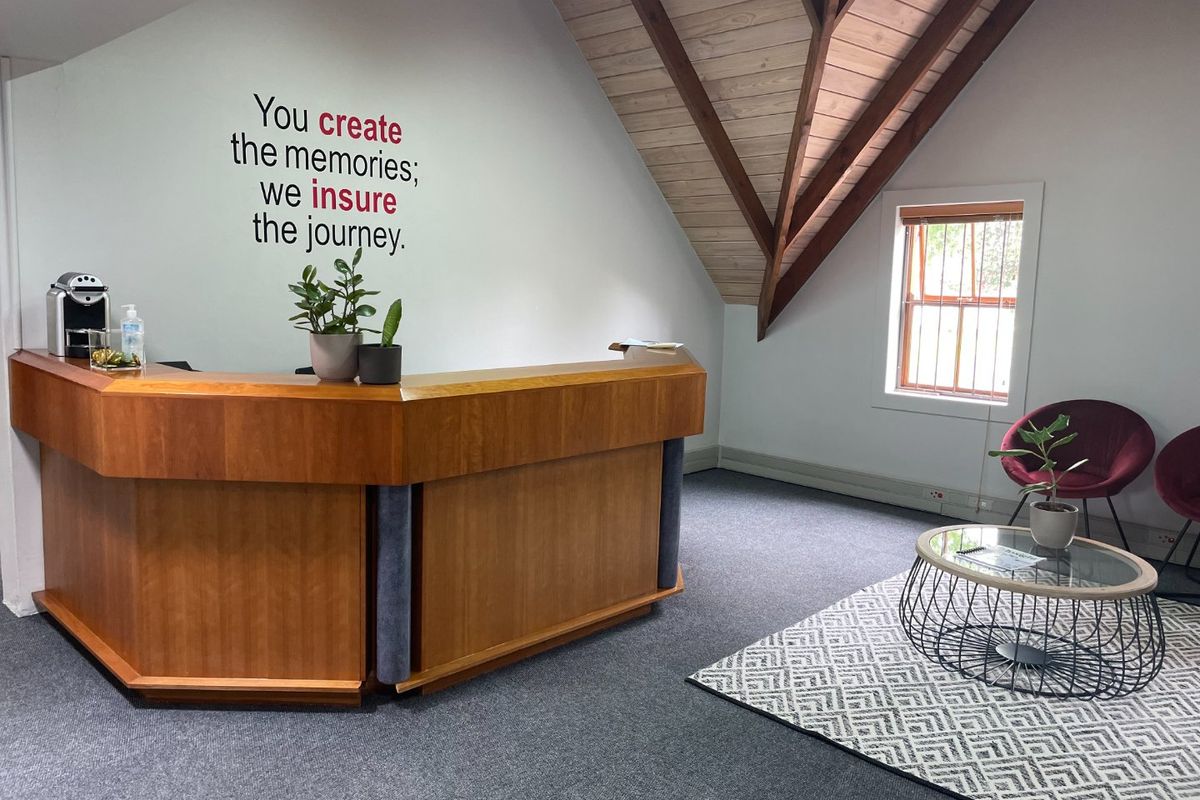 A professional office reception area featuring a built-in wooden desk, exposed timber roof trusses, and a bright window with natural light.