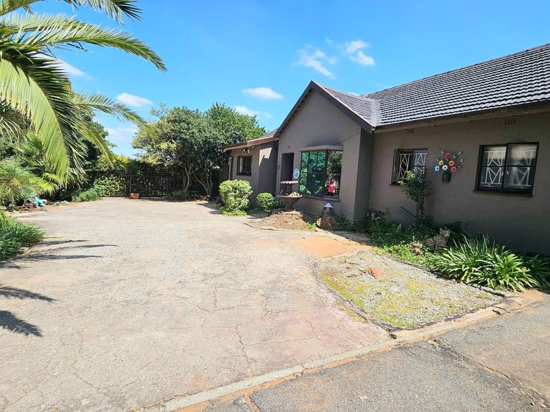 Front exterior view of a single-story house featuring a large concrete driveway, tiled roof, and established garden area.