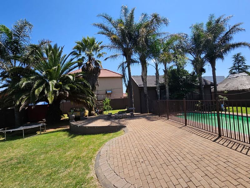 Outdoor pool area featuring a paved patio, fenced swimming pool, and established garden with mature palm trees.