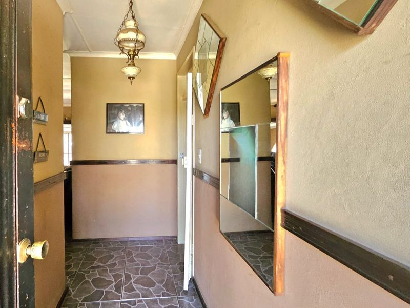A narrow hallway featuring tiled flooring, a dado rail, and a traditional pendant light fixture, requiring cosmetic updates to modernize the space.