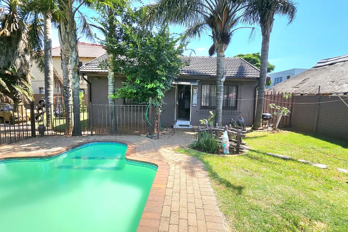 Rear exterior view featuring a swimming pool, paved patio area, and established garden with mature palm trees.