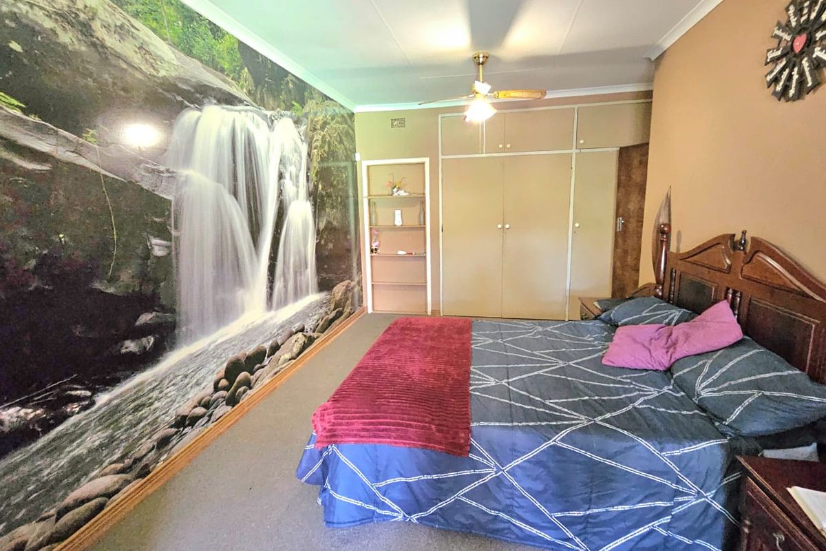Spacious bedroom featuring built-in cupboards, integrated shelving, and a ceiling fan, offering a functional layout with potential for modern updates.