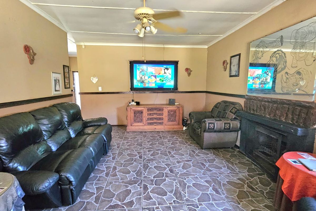 A living room featuring tiled flooring, a built-in fireplace, and a ceiling fan, with dated wall finishes and ceiling tiles.