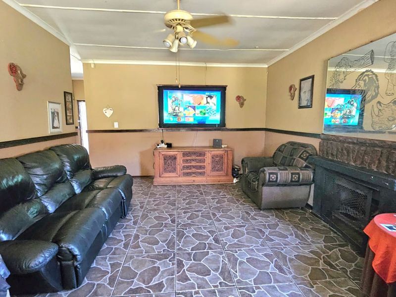 A living room featuring tiled flooring, a built-in fireplace, and a ceiling fan, with dated wall finishes and ceiling tiles.