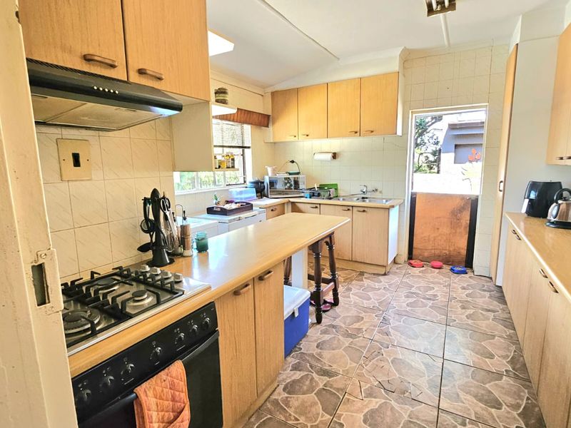 A functional kitchen featuring light wood cabinetry, a gas hob, oven, and tiled flooring, offering a practical layout with direct access to the exterior.