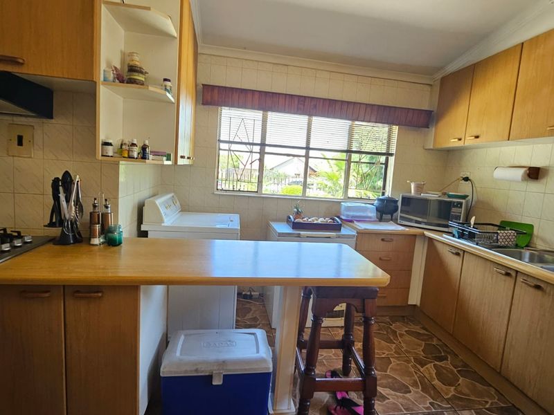 A functional kitchen featuring wooden cabinetry, a gas hob with extractor, and a double stainless steel sink with tiled backsplash.