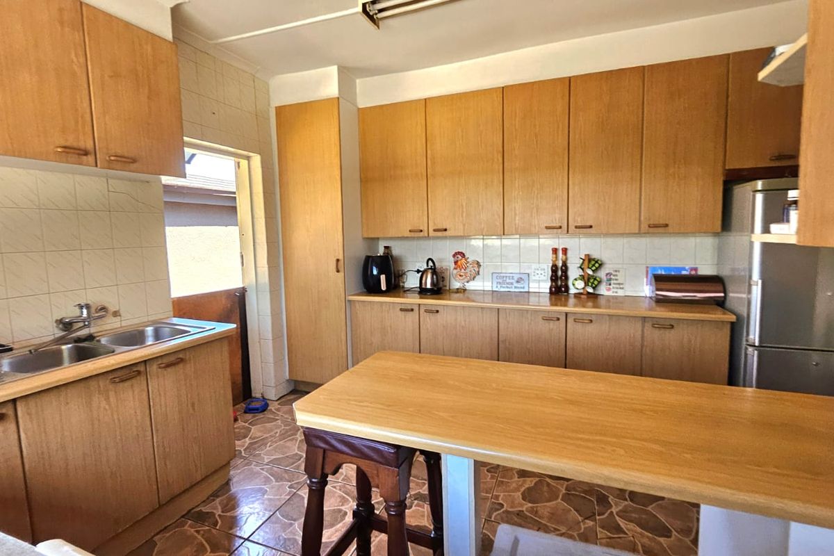 A functional kitchen featuring wood-look laminate cabinetry, tiled flooring, a double bowl sink, and a convenient breakfast bar area.
