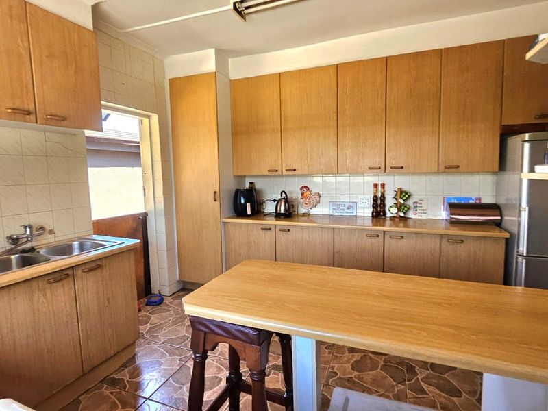 A functional kitchen featuring wood-look laminate cabinetry, tiled flooring, a double bowl sink, and a convenient breakfast bar area.