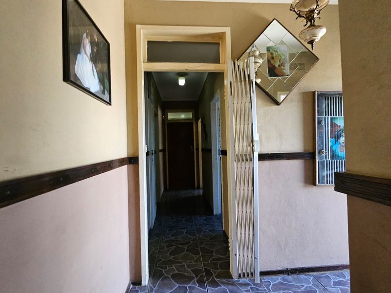 A hallway featuring tiled flooring, a security gate, and a transom window above the doorway, showing signs of wear and dated finishes.