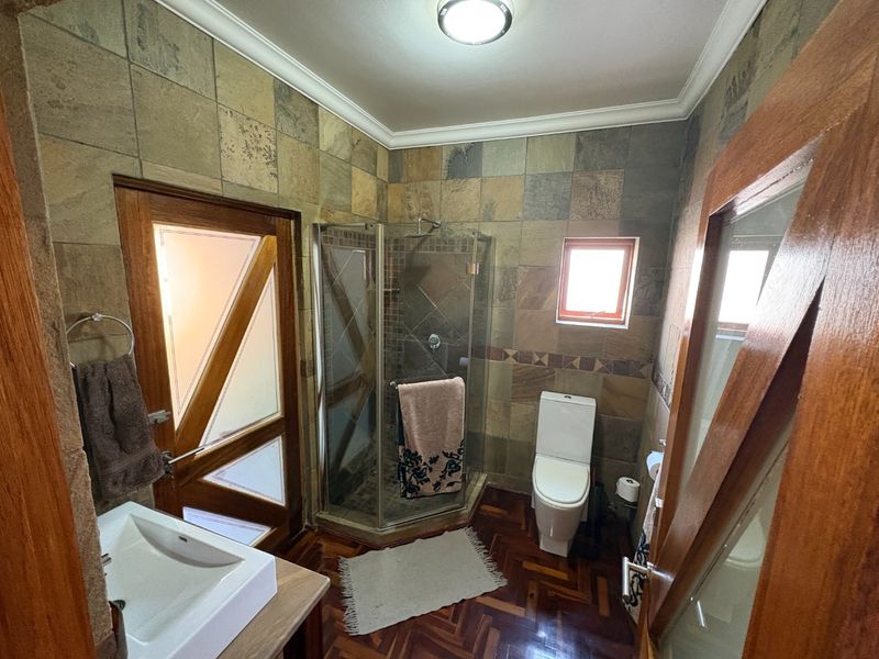A bathroom featuring parquet flooring, stone-look wall tiles, a corner shower enclosure, and a vessel sink with wooden door frames.
