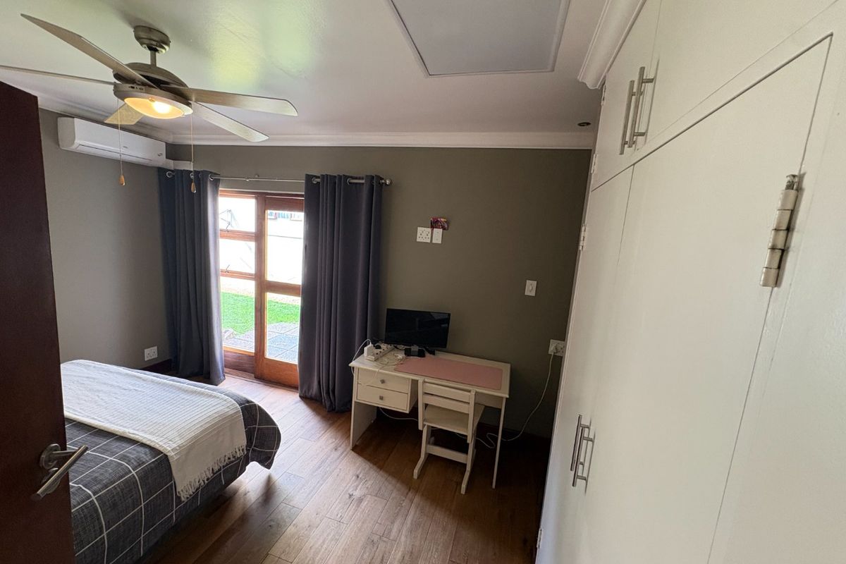 A well-maintained bedroom featuring timber-look flooring, built-in cupboards, a ceiling fan, and direct access to the garden through a timber-framed glass door.