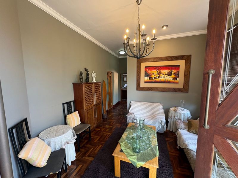 A cozy living room featuring classic parquet flooring, decorative cove cornicing, and a central chandelier, creating a warm and inviting atmosphere.