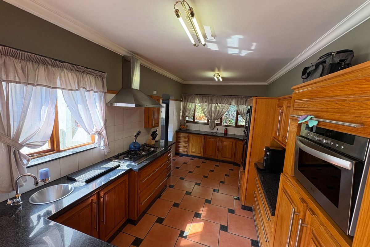 Spacious kitchen featuring wooden cabinetry, granite countertops, a gas hob with extractor fan, built-in oven, and tiled flooring.
