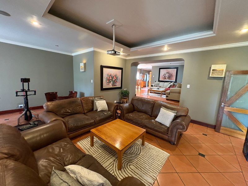 Spacious living room featuring terracotta floor tiles, a recessed ceiling with integrated lighting, and a ceiling-mounted projector, leading into an adjacent dining area.