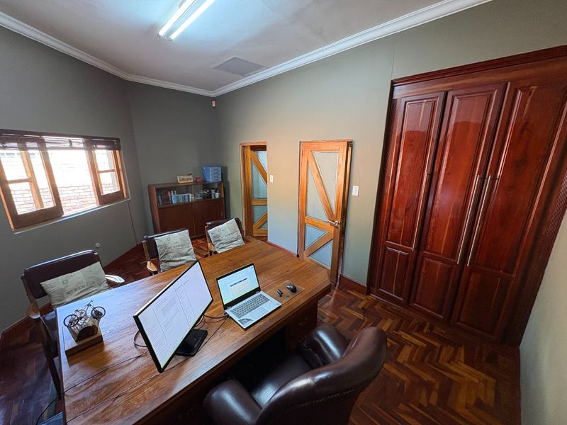 A well-maintained home office featuring rich parquet flooring, built-in wooden cabinetry, and classic wooden door frames, providing a professional and warm workspace.