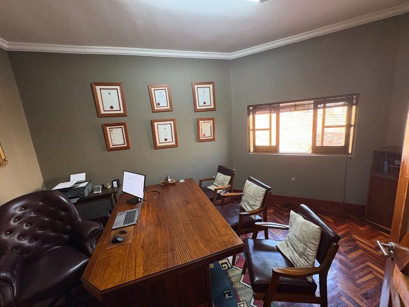 A dedicated home office featuring classic herringbone parquet flooring, crown molding, and natural light through wooden-framed windows.