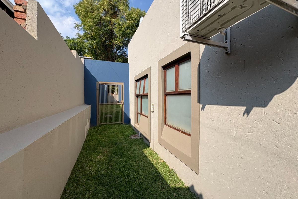 A side passage featuring a lawn, boundary walls, and a secure metal gate, with an exterior air conditioning unit mounted on the wall.