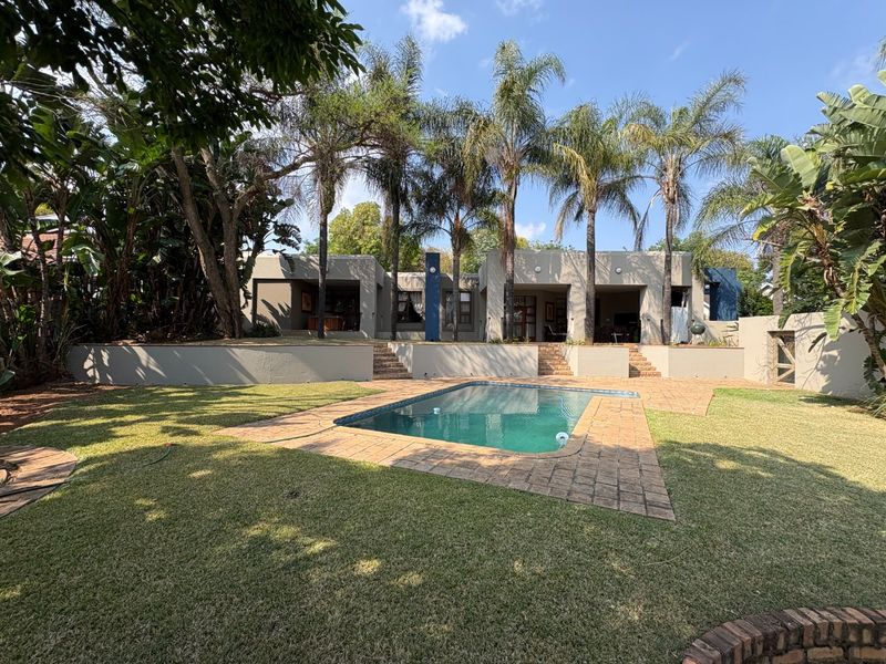 A well-maintained backyard featuring a swimming pool with brick paving, tiered retaining walls, stone steps, and a covered patio area.