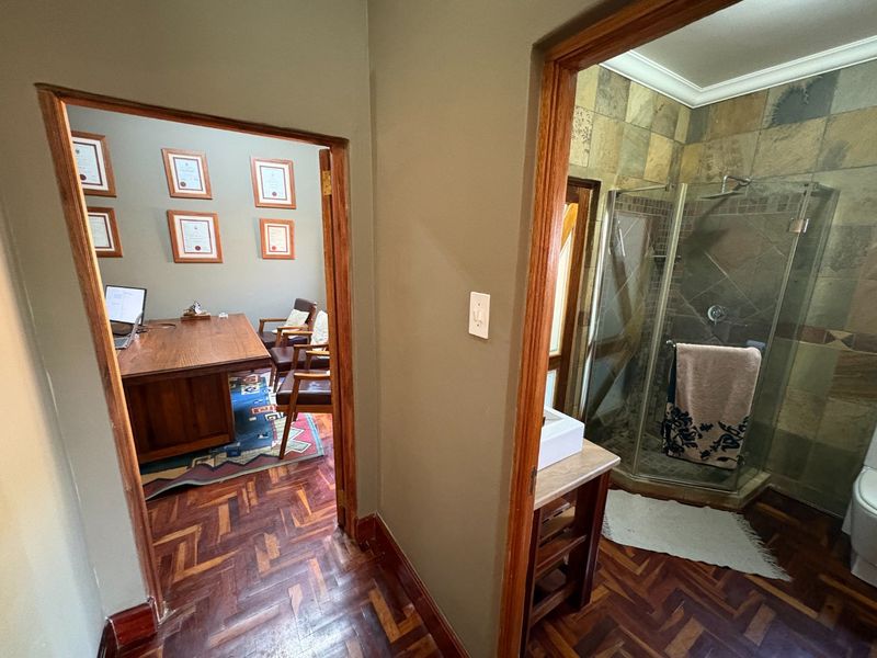 A hallway providing access to an office space and a bathroom featuring stone wall tiles and a glass shower enclosure.