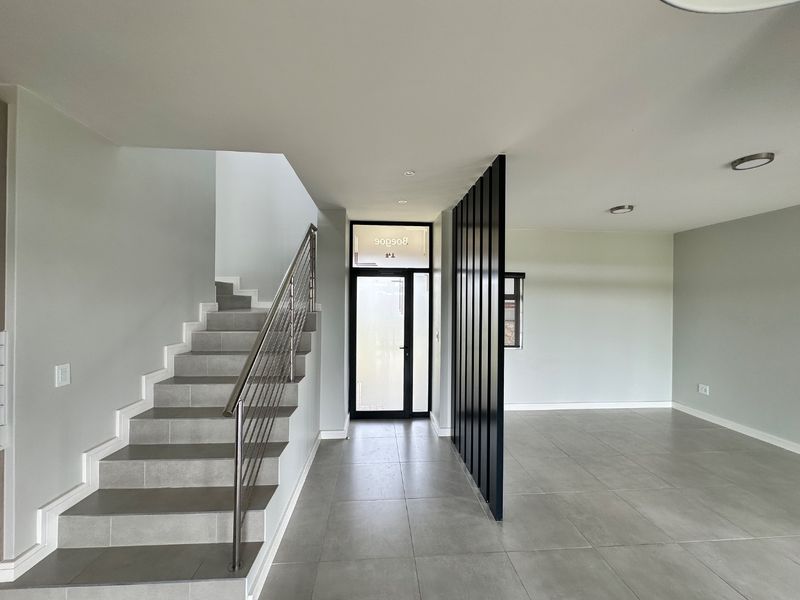 Modern entrance hall featuring a tiled staircase with stainless steel balustrade, large format floor tiles, and a contemporary vertical slat room divider.