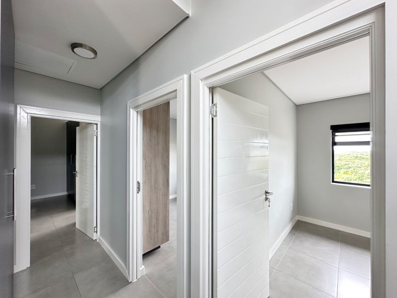 A bright, modern hallway featuring neutral grey walls, tiled flooring, and clean white door frames leading into adjacent rooms.
