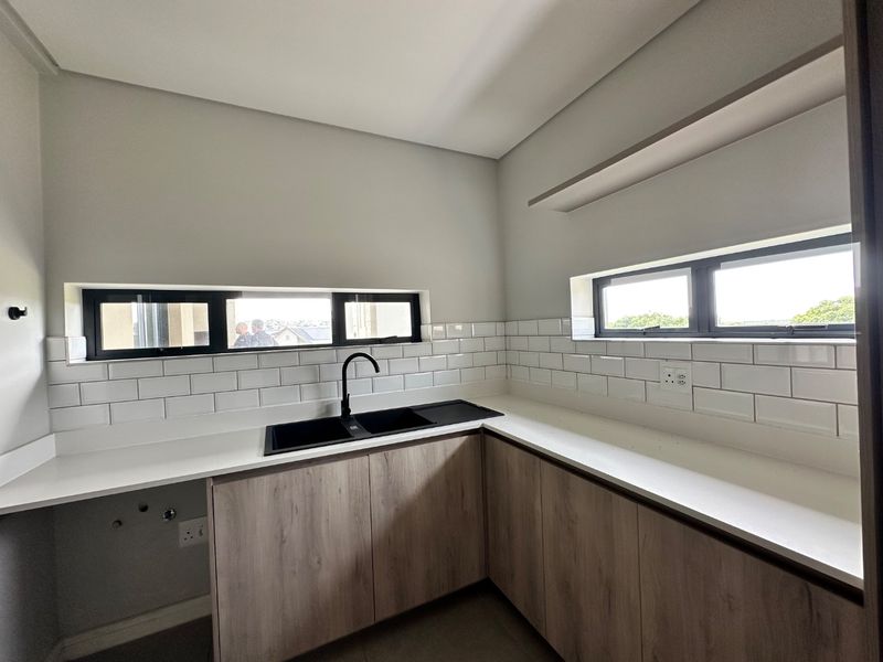 A modern, clean scullery featuring light wood-look cabinetry, white quartz countertops, a black sink with matching tap, and a classic white subway tile backsplash.