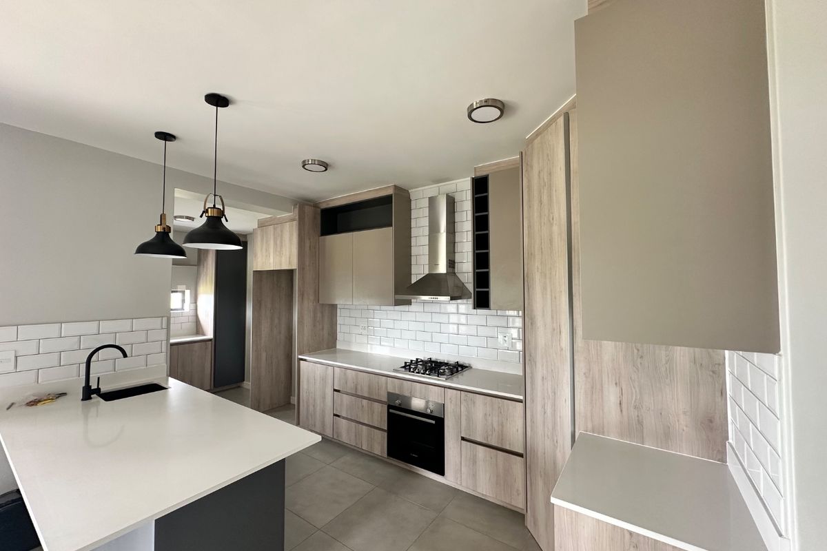 Modern kitchen featuring light wood-tone cabinetry, white quartz countertops, subway tile backsplash, a central island, and integrated stainless steel appliances.