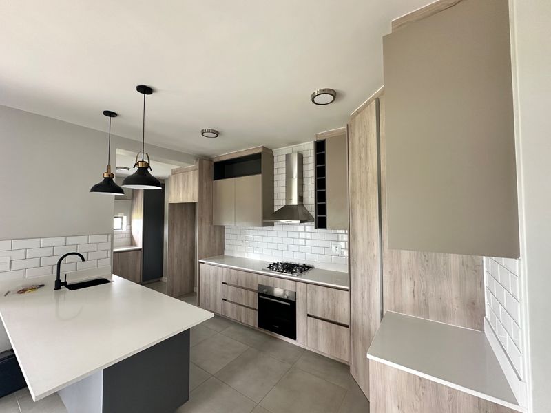Modern kitchen featuring light wood-tone cabinetry, white quartz countertops, subway tile backsplash, a central island, and integrated stainless steel appliances.