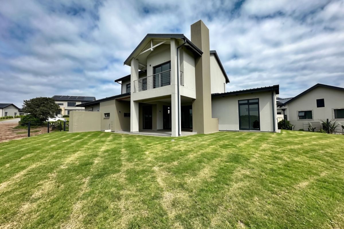 Rear view of a modern two-story house featuring a covered patio, upper-level balcony, chimney, and a well-maintained lawn.