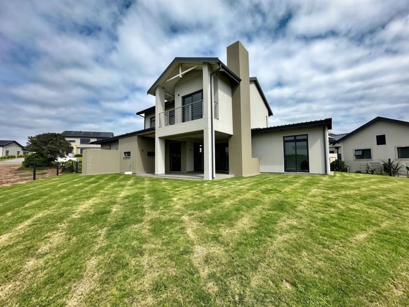 Rear view of a modern two-story house featuring a covered patio, upper-level balcony, chimney, and a well-maintained lawn.