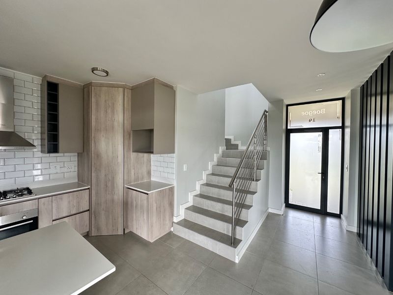 Modern open-plan kitchen featuring light wood cabinetry, subway tile backsplash, and integrated appliances, adjacent to a tiled staircase and main entrance.
