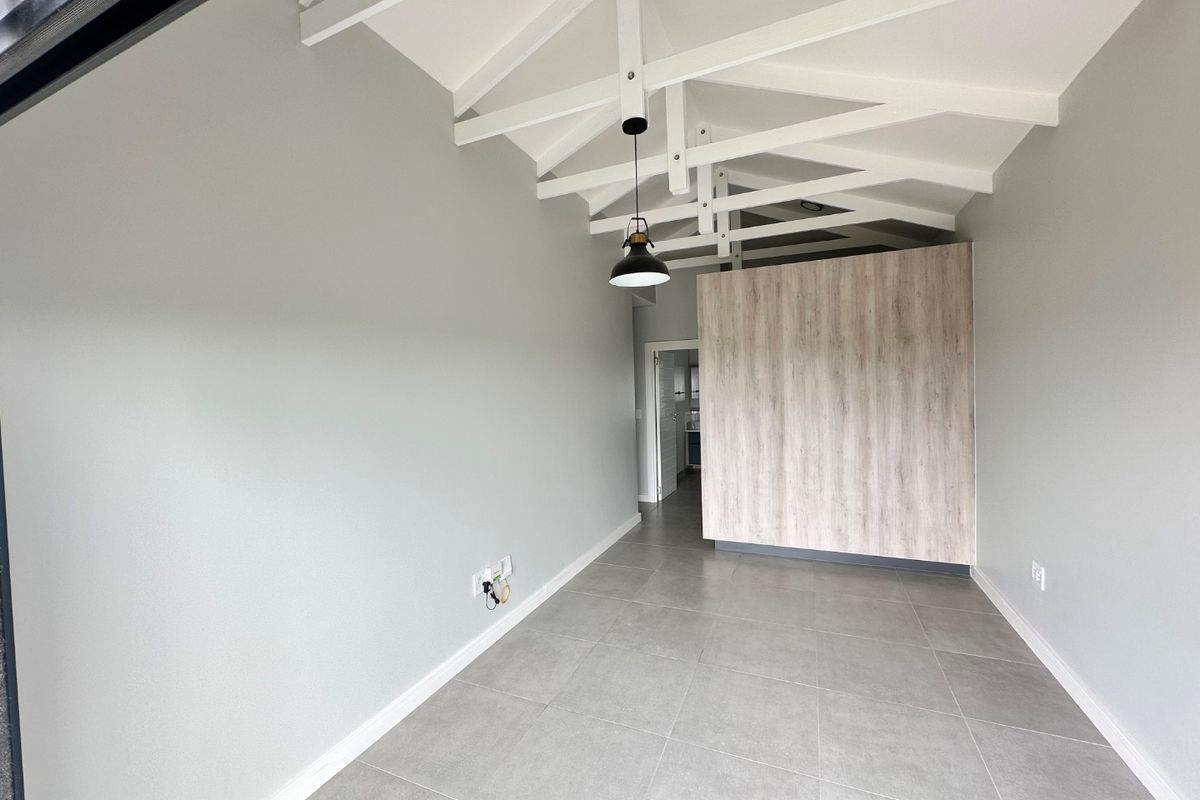 A bright, modern living area featuring exposed white timber trusses, large format grey floor tiles, and a contemporary wood-look feature wall.