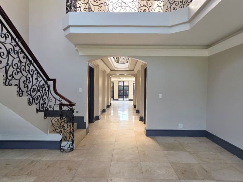 Spacious grand entrance hall featuring stone tile flooring, an elegant wrought iron staircase, and an arched walkway leading to the rear of the home.
