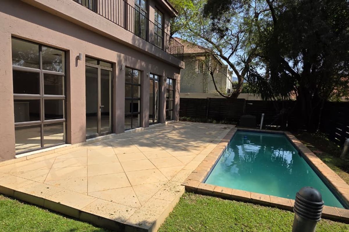 Rear exterior view featuring a paved patio area, a swimming pool, and large glass doors leading into the main living space.