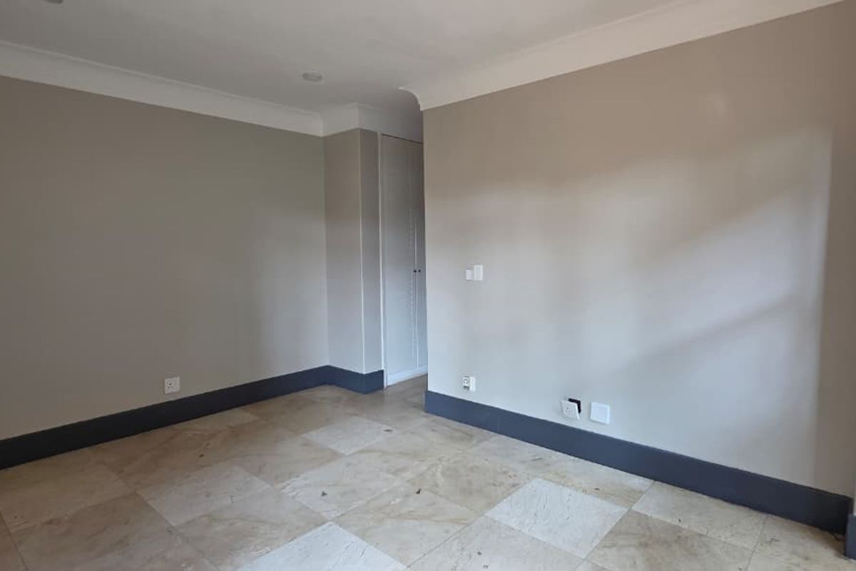 An empty bedroom featuring neutral wall paint, stone tile flooring, and a built-in cupboard with classic cornice detailing.