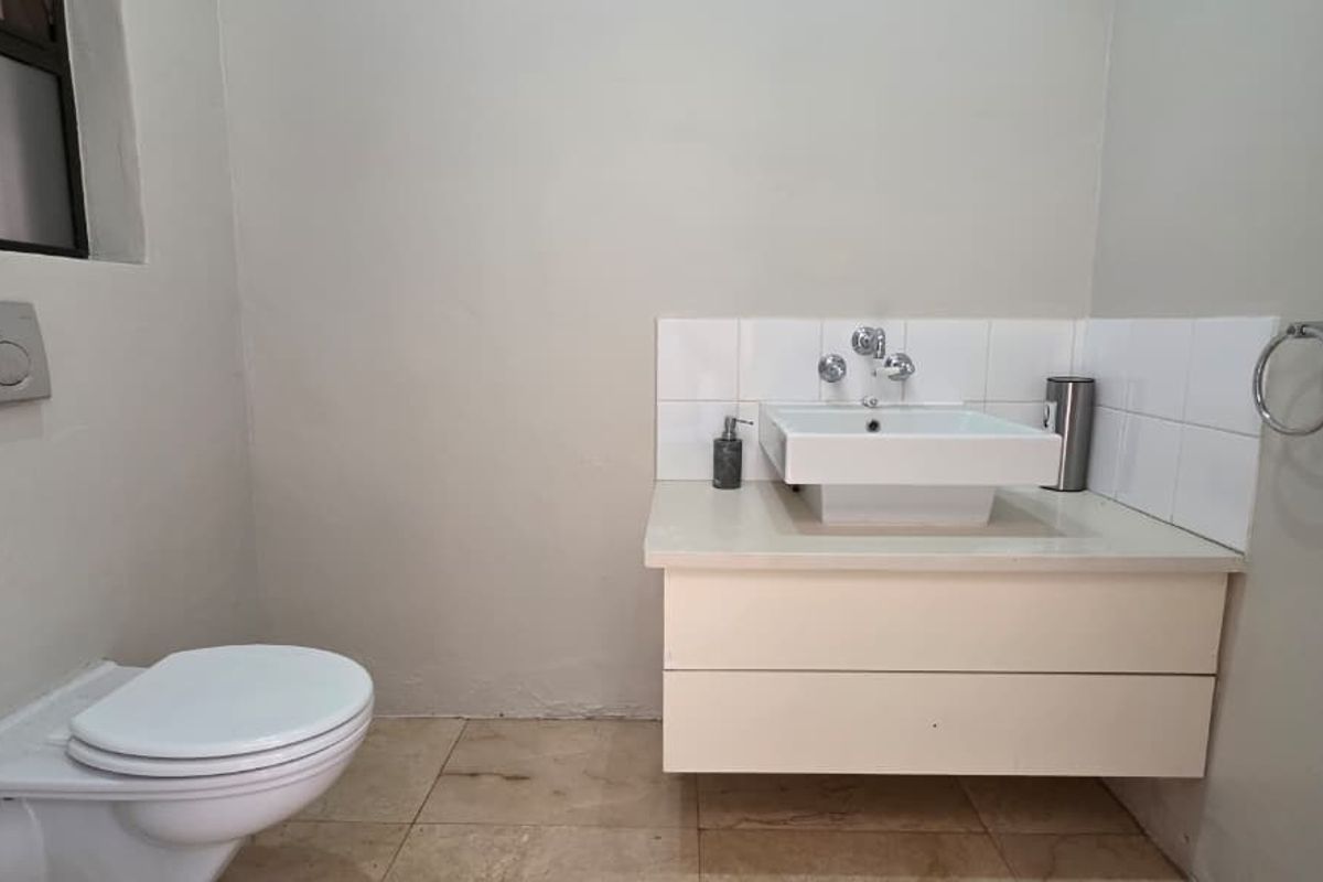 A functional bathroom featuring a wall-hung toilet with a concealed cistern and a modern vanity unit with a vessel sink.