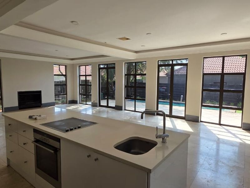 Spacious open-plan living area featuring a modern kitchen island with built-in appliances, tiled flooring, and large windows overlooking the pool area.