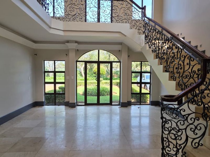 Spacious double-volume entrance hall featuring elegant wrought iron staircase railings, stone tile flooring, and large arched glass doors overlooking the garden.