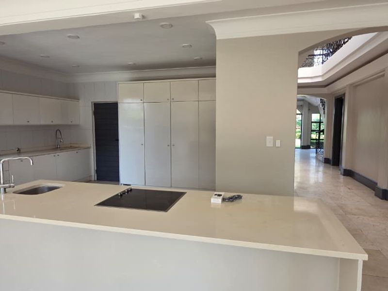 Spacious open-plan kitchen featuring a central island with integrated hob, stone countertops, ample built-in cabinetry, and elegant stone flooring throughout.