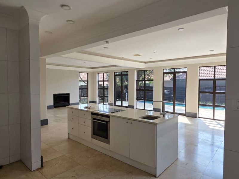 Spacious open-plan kitchen and living area featuring a central island with built-in appliances, fireplace, and large glass doors leading to the pool area.