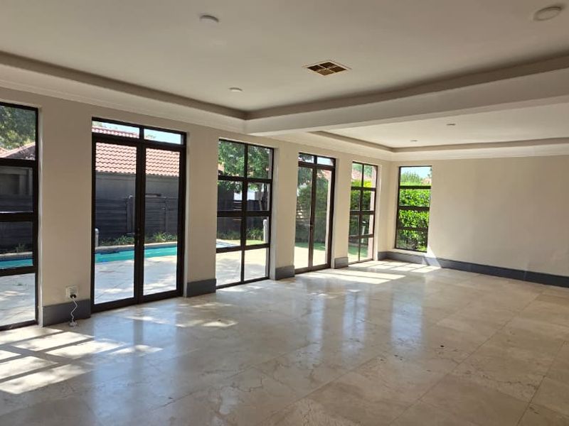 Spacious open-plan living area featuring polished travertine floors, recessed lighting, and expansive glass doors providing seamless access to the pool area.