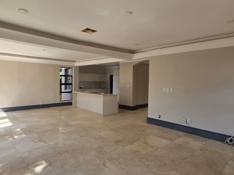 Spacious open-plan living area featuring travertine flooring, recessed ceilings with downlights, and a central kitchen island, offering a bright and versatile layout.