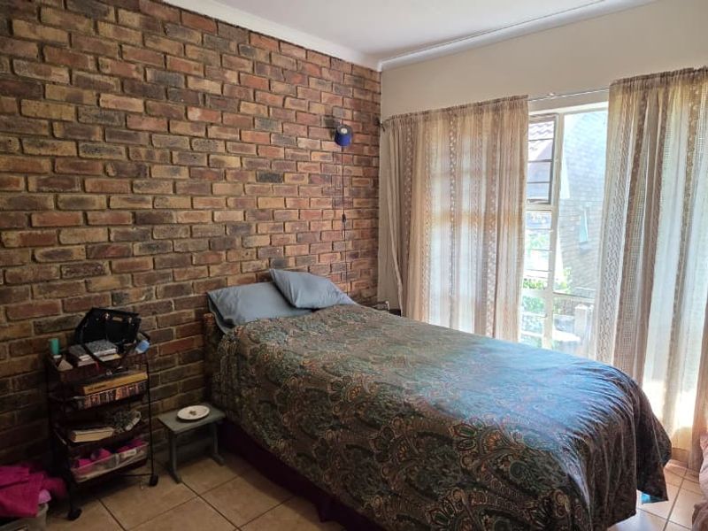 A bedroom featuring a rustic exposed brick feature wall, tiled flooring, and large windows allowing for natural light.
