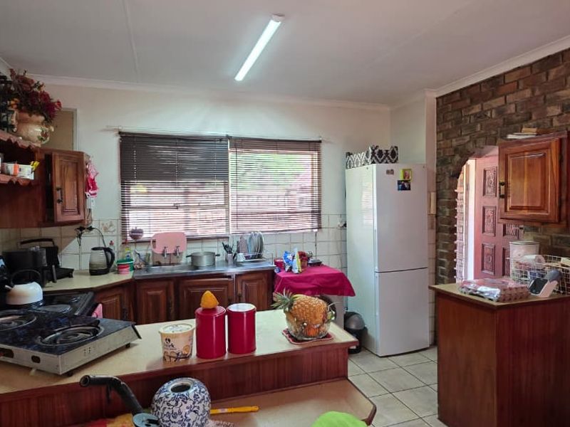 A functional kitchen featuring wooden cabinetry, tiled splashbacks, and a distinctive exposed brick wall with an arched entryway leading to adjacent spaces.