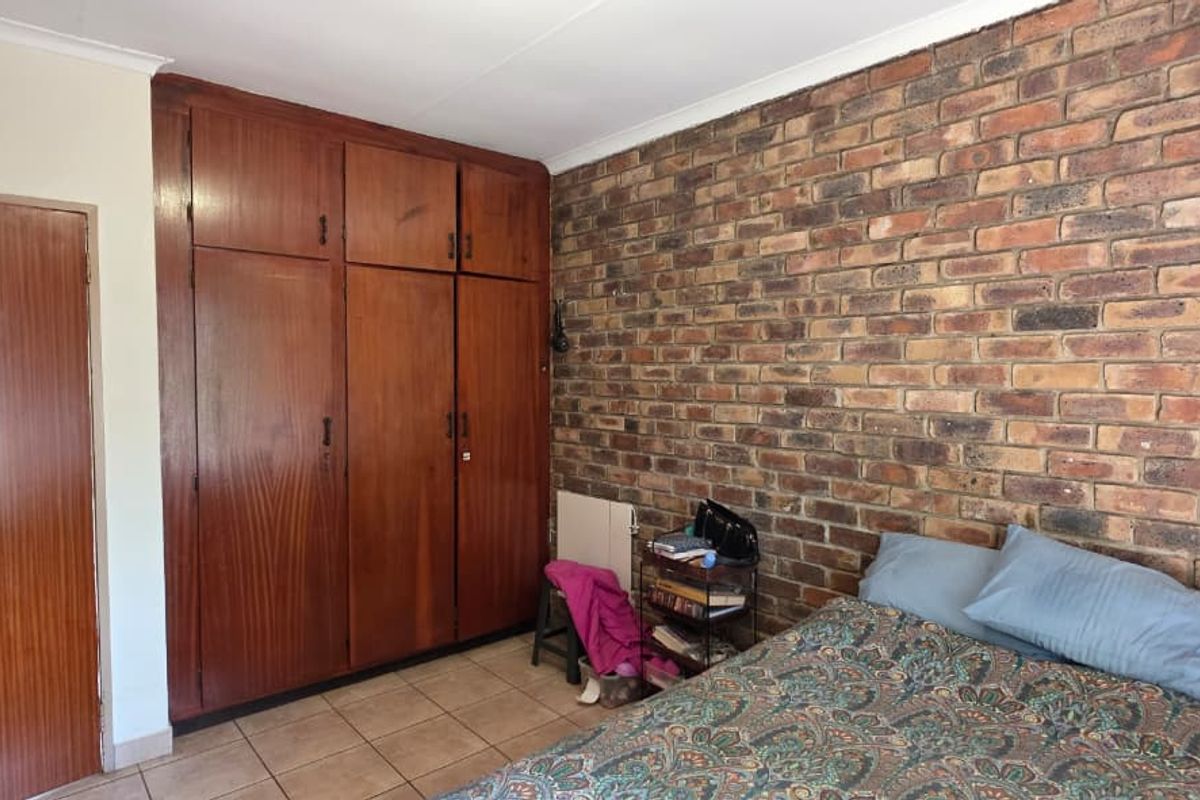A bedroom featuring a prominent exposed brick wall, tiled flooring, and extensive built-in wooden cabinetry for storage.