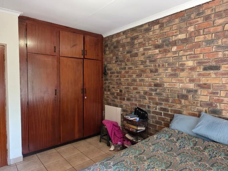 A bedroom featuring a prominent exposed brick wall, tiled flooring, and extensive built-in wooden cabinetry for storage.